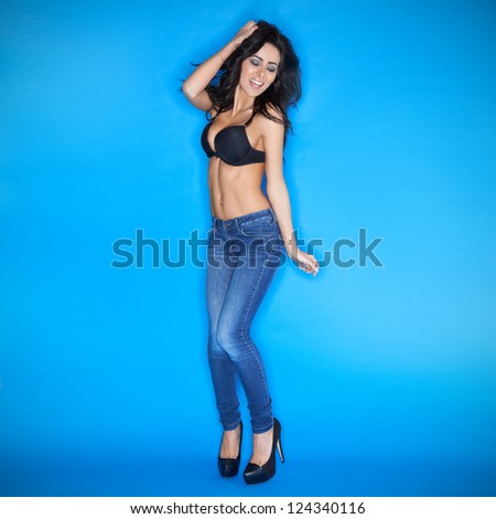 Happy sexy party woman with a vivacious smile and beautiful body dancing and jiving in tight fitting jeans and stilettoes on a blue background