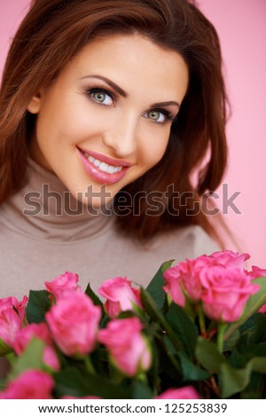 Gorgeous brunette woman with beautiful big eyes holding a bunch of romantic pink roses