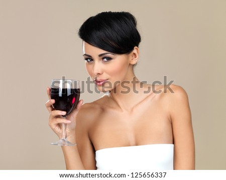 Beautiful seductive woman drinking red wine from a large wineglass, head and shoulders portrait isolated on a beige studio background