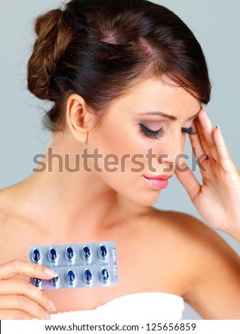 Beautiful young woman with a bad headache holding her hand to her forehead and a blister pack of pills in the other
