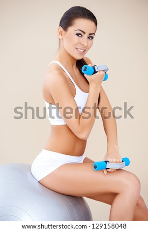 Pretty woman training muscles with dumbbells while balancing on fitness ball