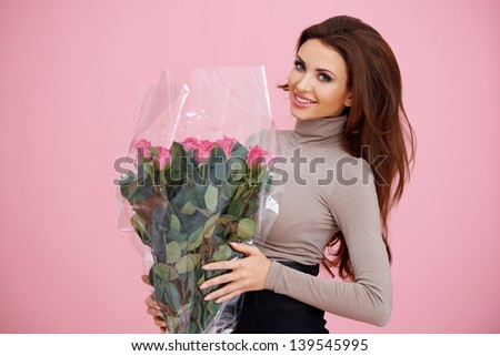 Happy beautiful woman holding a large bouquet of cellophane wrapped pink roses for Valentines Day   birthday or anniversary on a pink background