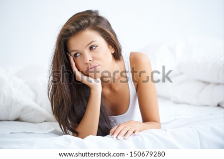 Brunette woman lying on white bed in bad mood
