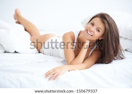Smiling beautiful woman relaxing in bed enjoying a lazy day and looking at the camera with a radiant smile
