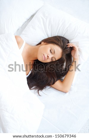 Serene young woman sleeping peacefully in bed dreaming sweet dreams  high angle portrait