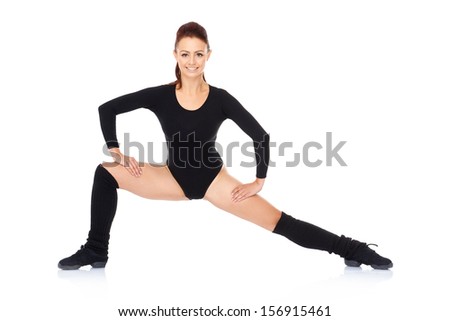 Fit healthy beautiful woman working out in a black leotard standing with outstretched legs and arms smiling at the camera  over a reflective white surface
