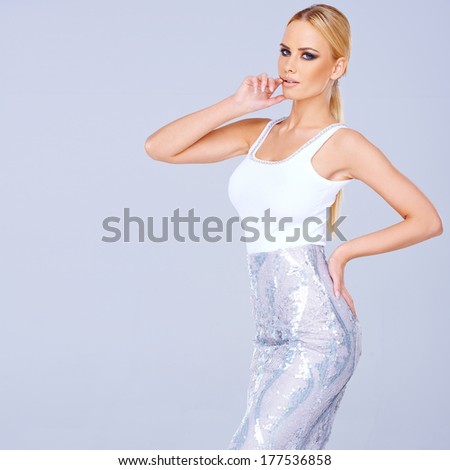 Tall elegant blond woman in a stylish slim line skirt standing posing with her hands on her hips on a blue-grey background