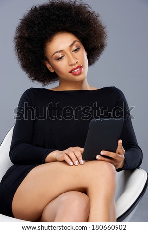 Beautiful elegant African American businesswoman sitting reading her tablet in a comfortable modern design armchair