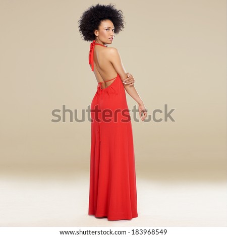 Elegant African American woman with an afro hairstyle posing in a red evening gown standing sideways looking over her shoulder