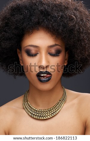 Beautiful seductive African American woman with bare shoulders wearing a gold choker posing with her lips parted and the tip of her tongue showing and downcast eyes