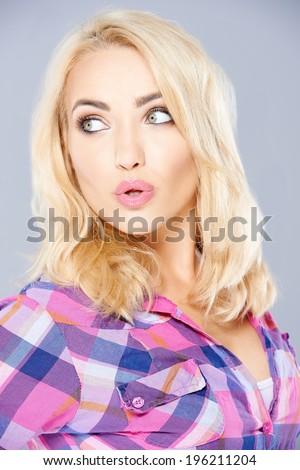 Sexy woman with shoulder length blond hair pouting her lips in admiration as she looks back over her shoulder  on grey