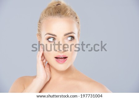 Beautiful young blonde woman looking surprised staring wide eyed at the camera with her lips parted  face portrait on grey