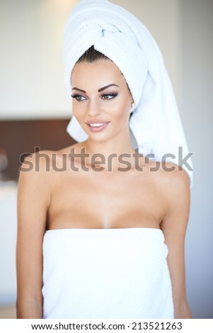 Serene thoughtful beautiful woman with her hair and body wrapped in white towels looking dreamily off to the left of the frame