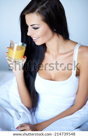 Young woman enjoying a healthy glass of orange juice as she relaxes in bed in the morning after a refreshing nights sleep