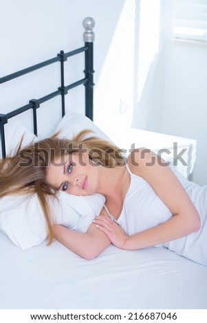 Young woman enjoying a lazy day in bed relaxing under the bed clothes with a shaft of sunlight coming through the window behind her