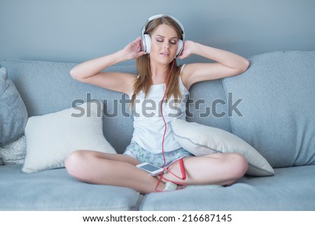 Beautiful woman enjoying her music library sitting cross-legged on a sofa wearing headphones with a look of enjoyable bliss on her face