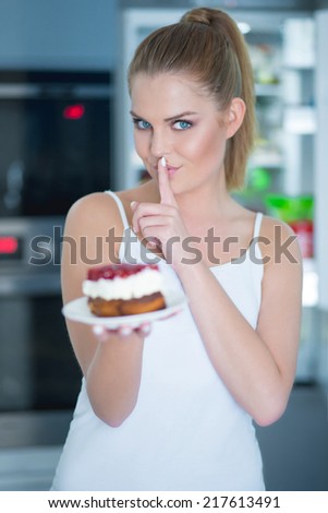 Guilty young woman preparing to eat a cake making a hushing gesture with her finger to her lips as she asks for secrecy