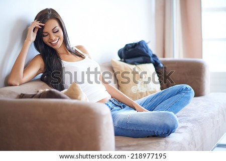 Pretty casual young woman enjoying a relaxing day at home reclining on a comfortable sofa with a happy smile