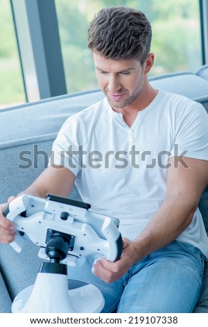 Middle Age Caucasian Man in White Shirt and Faded Blue Pants Playing His Cool Gadget at Home.