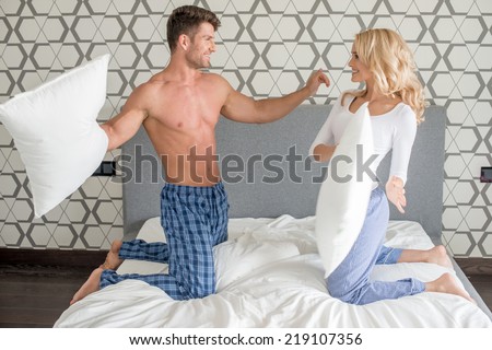 Attractive young couple in their sleepwear having a pillow fight as they kneel on their bed enjoying a relaxing day