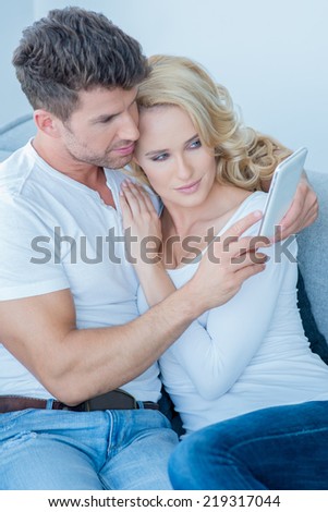 Loving couple reading an sms on a mobile phone as they relax together arm in arm on a sofa at home