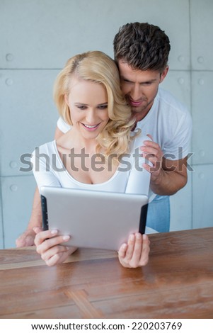 Young couple reading information on a tablet computer with the attractive blond wife sitting at a table with her husband reading over her shoulder