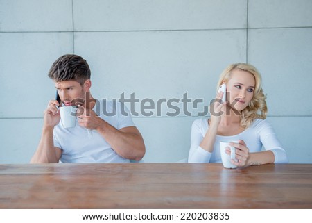 Couple both using their mobile phones simultaneously as they sit at a wooden counter enjoying their morning coffee