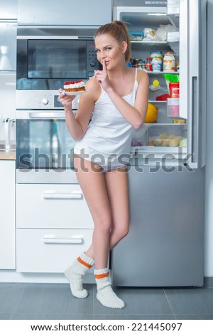 Naughty young woman stealing cake from the fridge making a shushing gesture as she asks for secrecy to hide her guilt