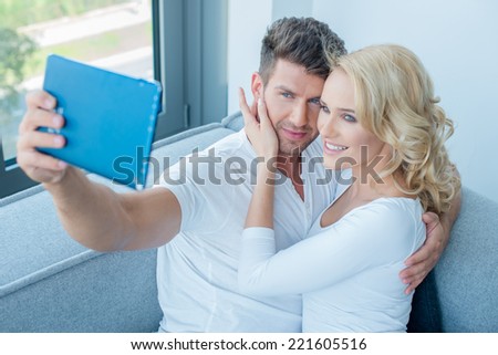 Pretty Young White Couple in White Taking Self Photos Using Blue Tablet Inside Home.