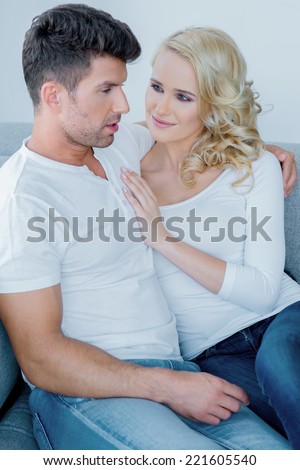 Young couple relaxing together on a sofa with the beautiful blond wife snuggling up to her husband with a smile