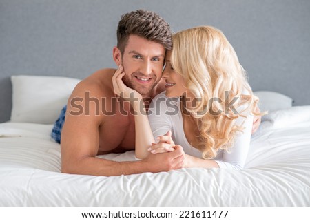 Sweet Smiling Young White Couple Lying on White Bed. Isolated on Gray Background.