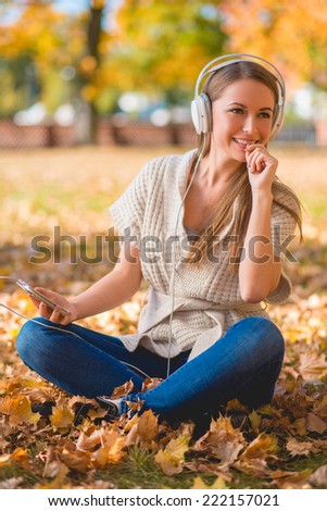 Happy young woman relaxing with her music sitting on the ground in a colorful autumn park listening to her headphones with a smile