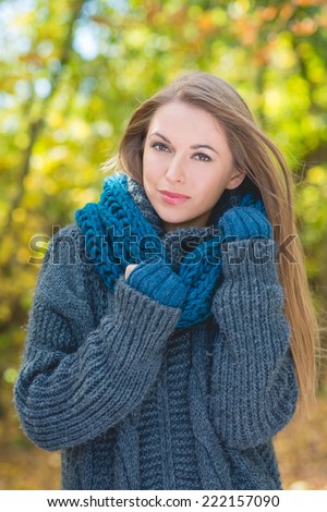 Trendy woman in warm autumn fashion snuggling down into her blue polo neck jersey and scarf while walking outdoors in a park