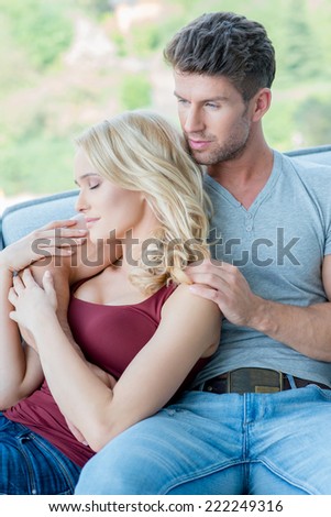 Young couple enjoying a relaxing day with the beautiful young blond wife lying back in her husbands arms with closed eyes as they sit together on the sofa