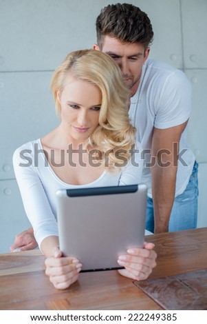 Beautiful woman reading information on a tablet computer as she sits at a table with her husband looking over her shoulder