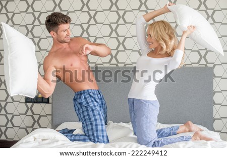 Playful attractive young couple having a pillow fight as they kneel on their bed in their sleepwear smiling and laughing