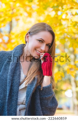 Young woman dressed in warm woollen jersey and mittens standing looking down at the camera with a a smile in a colorful autumn garden