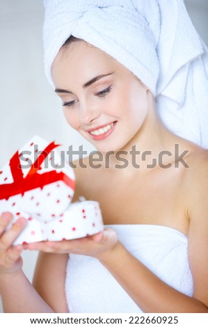 Young woman with her hair and body wrapped in fresh clean white towels opening a heart-shaped gift box with a look of anticipation and pleasure