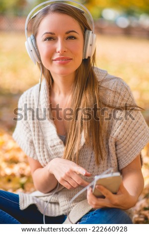 Attractive woman listening to her music library on her MP3 player as she sits on the ground in a park in autumn
