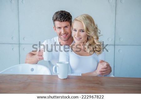 Sweet Smiling Young Couple in White Having Morning Coffee at Wooden Table. Isolated on White Wall Background. Captured Indoor.