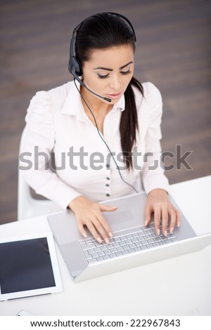 Virtual Customer Service Representative Using Head Set and Laptop with Ipad on Side Placed on White Table