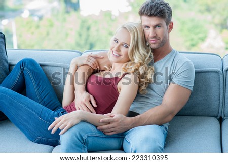 Young couple relaxing on a sofa together at home lying in each others arms with a beautiful blond woman and handsome unshaven man