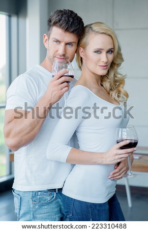Sexy attractive couple standing in a close embrace drinking red wine and smiling at the camera