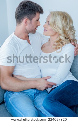 Young couple share a tender moment as they relaxing together on the sofa looking into each others eyes with love and passion