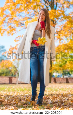 Pretty Blond Woman in Big White Coat  Perfect Outfit for Autumn  Holding Leaves While Seriously Facing on Right Frame with Hand on the Chin.