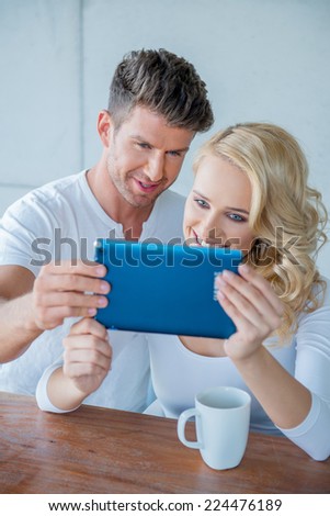 Couple smiling as they read a tablet computer together while they enjoy their morning coffee catching up on social media and morning news