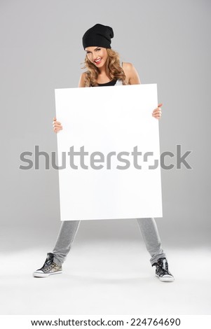 Cool Pretty Young Woman in Bonnet Holding White Board. Captured in Studio in Gray Background.