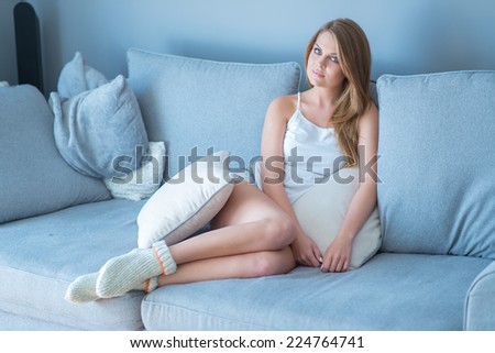 Sexy Young Blond Woman in White Sleeveless and Socks on Light Blue Gray Couch. Captured Indoor.
