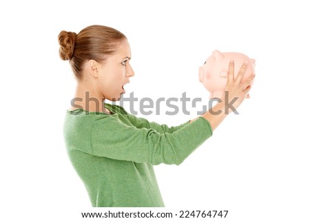 Shocked Young Woman in Green Long Sleeves Shirt Facing Pink Piggy Bank  Captured in Side View. Isolated on White Background.