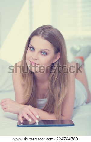 Pretty Long Hair Female Lying on Bed Playing with Tablet with Crossed Legs at the Back. Captured Indoor.